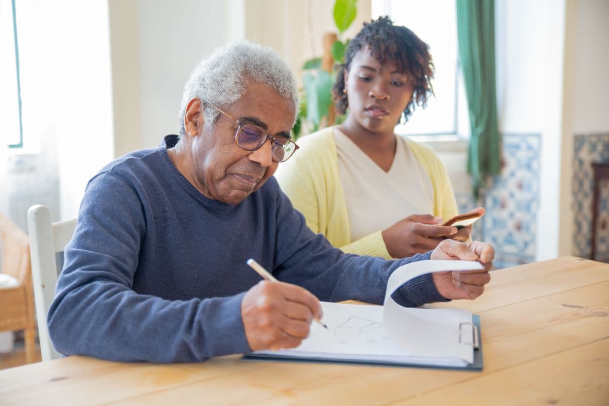 An older man completing paperwork at home with his adult daughter